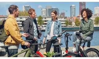 Two men and two women laugh while enjoying a view of the river city of Rotterdam alongside their eBikes, unmounted