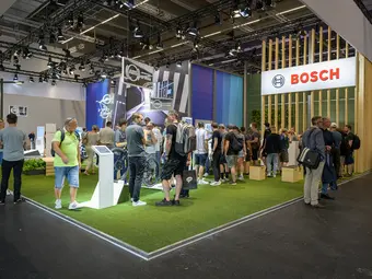 Several individuals are gathered at a Bosch trade show booth. The floor is covered with artificial turf, and the booth features a modern design.