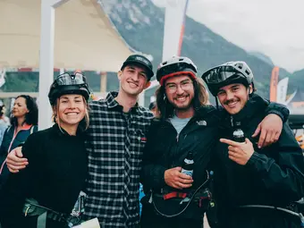 Four eBike riders have their hands around their shoulders and are looking into the camera with a smile, two of them have beer bottles in their hands.