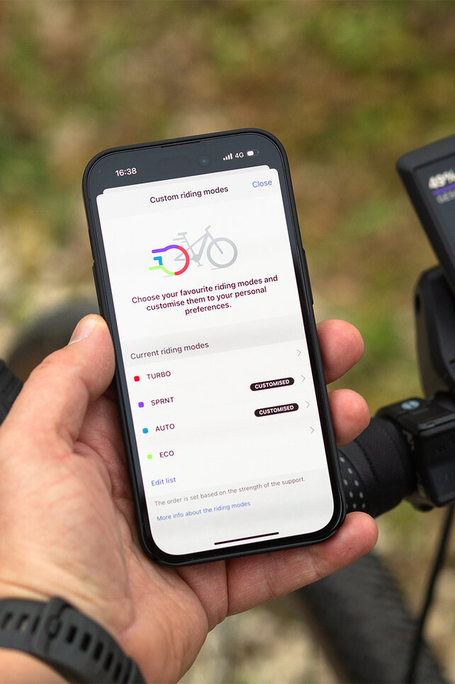 Close-up van een stuur met Kiox 500 en smartphone, waarop de rijmodi zijn gepersonaliseerd.