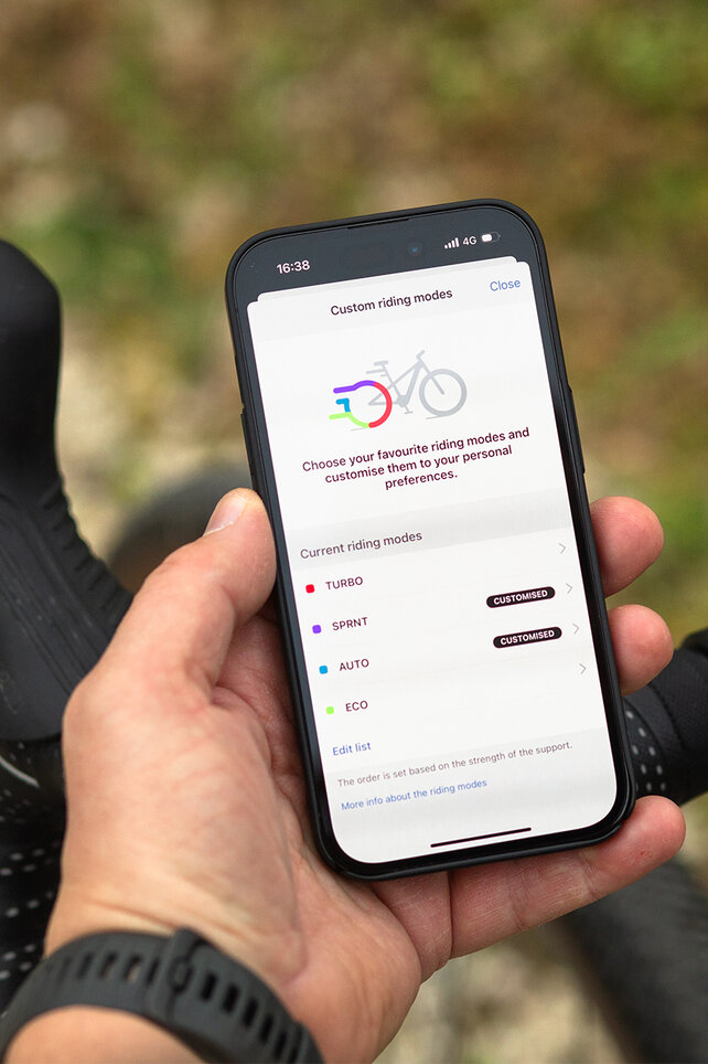 Primo piano di un manubrio con Kiox 500 e smartphone, su cui vengono personalizzate le modalità di guida.