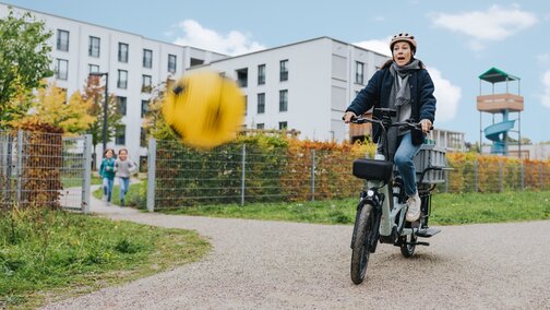 A woman suddenly brakes on her eCargo bike when a yellow ball bounces into the air in front of her. She looks startled.