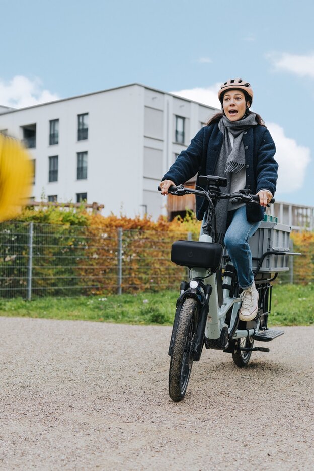 En kvinna bromsar plötsligt med sin eCargo-bike när en gul boll studsar upp i luften framför henne. Hennes blick är skrämd.