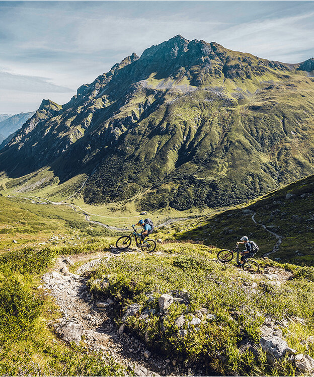 Två elcyklister tar sig igenom Alperna längs Heckmair-rutten, omgivna av bergslandskap och branta stigar.