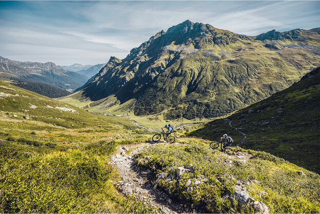 Deux cyclistes électriques parcourent la route Heckmair à travers les Alpes, entourés de paysages montagneux et de sentiers escarpés.