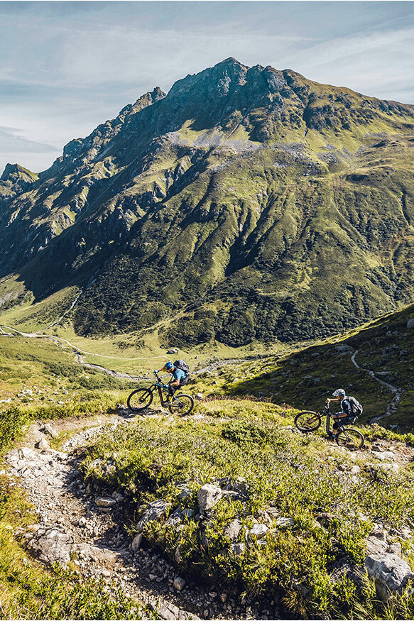 Two eBikers are riding the Heckmair route through the Alps, surrounded by mountain landscapes and steep trails.