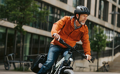A man in an orange jacket riding an eBike through the city