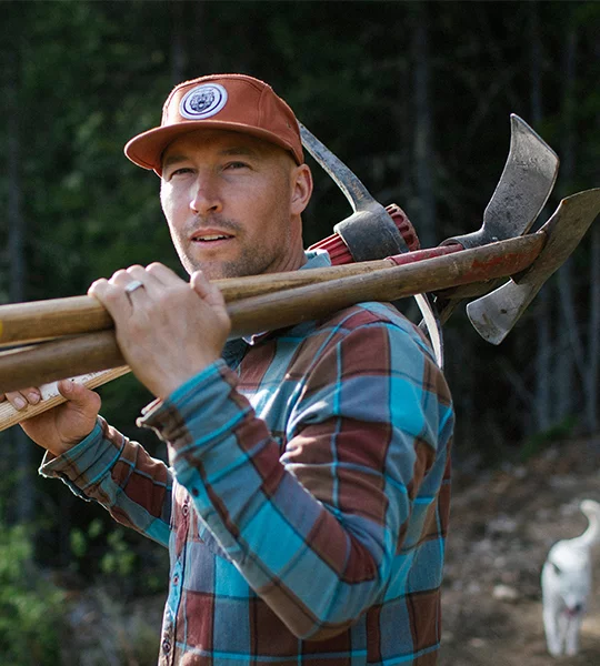 A man in a plaid shirt holding several pick axes over his shoulder