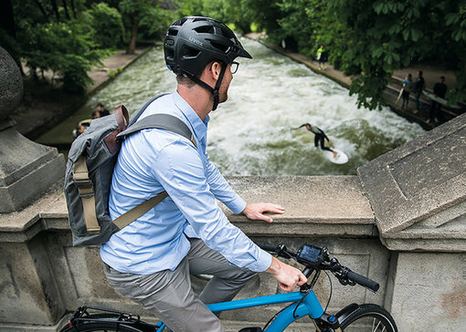 An eBike rider stopped on a bridge watching a surfer in the river below