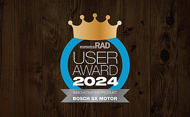 Icon with the text "nimms Rad User Award 2024": A bronze crown above the text, surrounded by a blue circle. Below it reads "BOSCH SX MOTOR - MOST INNOVATIVE PRODUCT". The background has a dark wood finish.