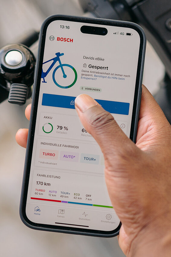 Eine Person hält ihr Smartphone mit geöffneter eBike Flow App auf der Startseite in der Hand. Im Hintergrund erkennt man den Lenker eines eBikes.