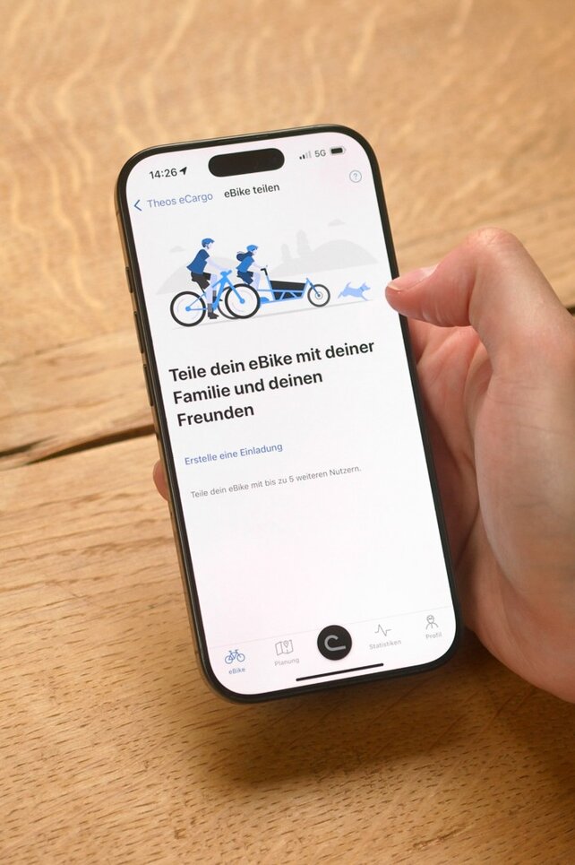 Eine Person sitzt am Tisch und hat die eBike Flow App an ihrem Smartphone geöffnet, um ihr eBike mit jemandem zu teilen.