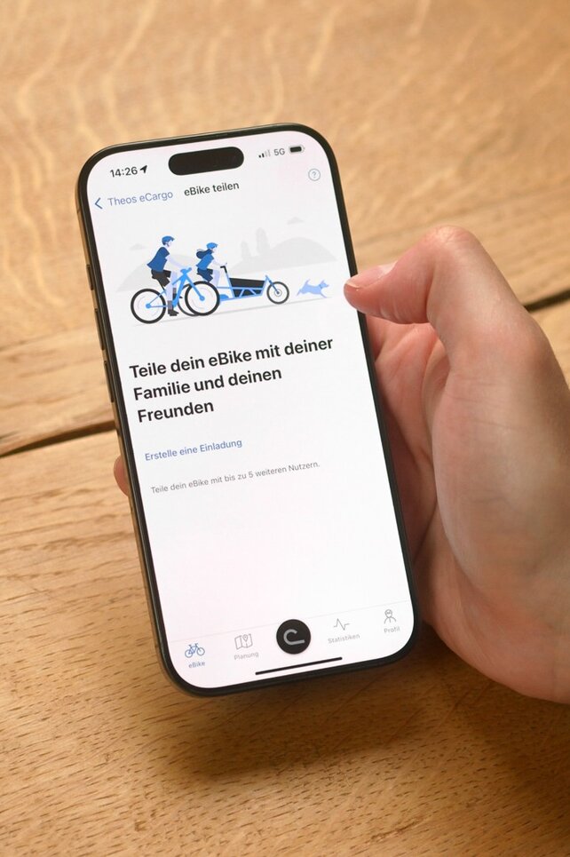 Eine Person sitzt am Tisch und hat die eBike Flow App an ihrem Smartphone geöffnet, um ihr eBike mit jemandem zu teilen.
