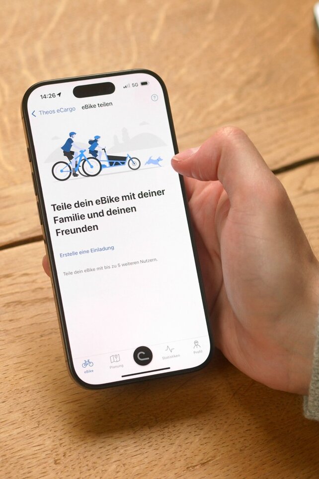Eine Person sitzt am Tisch und hat die eBike Flow App an ihrem Smartphone geöffnet, um ihr eBike mit jemandem zu teilen.