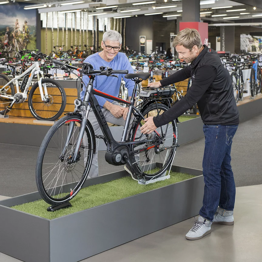 Un consultor de eBike de Bosch está con un hombre en una tienda de bicicletas, de pie frente a una bicicleta de exposición, y le explica sus características.