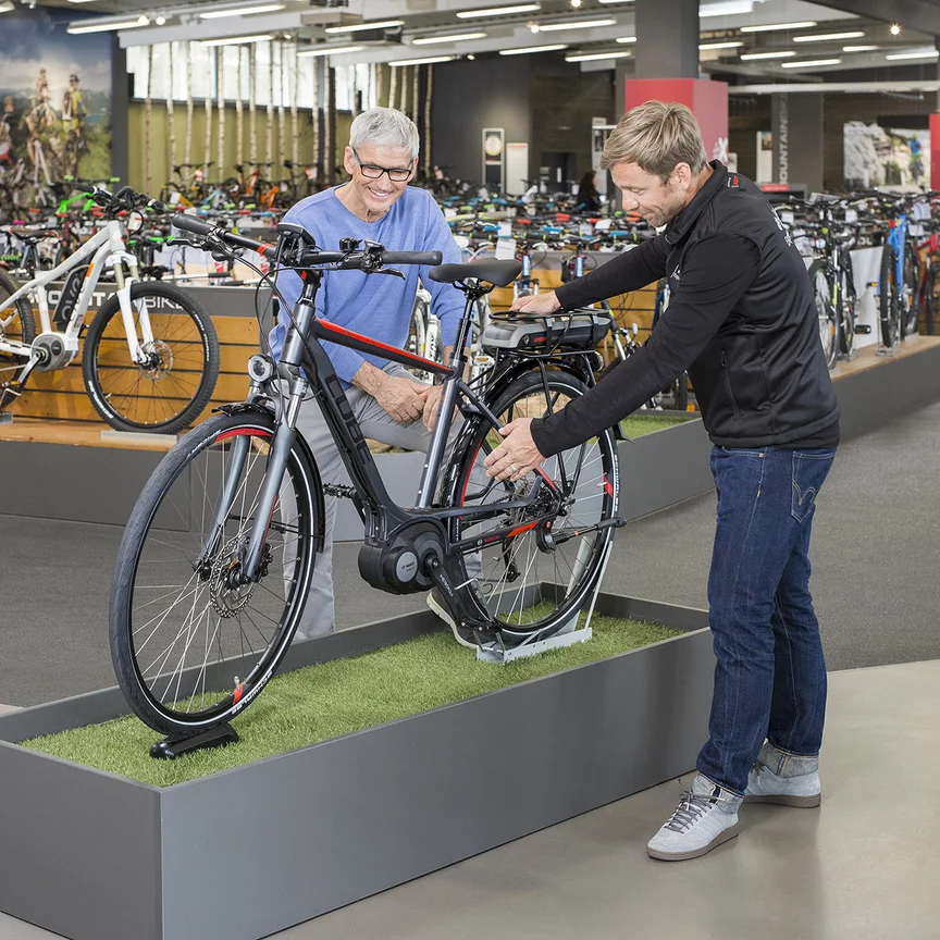 Un consultant Bosch VAE se tient avec un homme devant un vélo d’exposition dans un magasin de vélos et lui explique les caractéristiques.