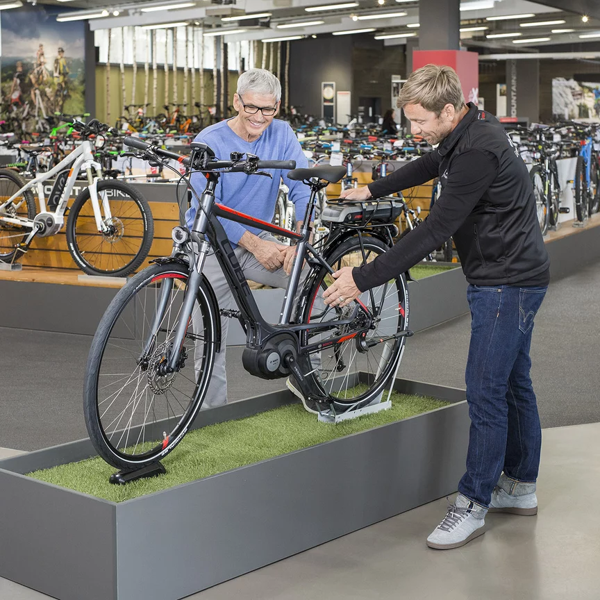 En Bosch eBike-konsulent står sammen med en mann i en sykkelbutikk foran en utstillingssykkel og forklarer den for ham.