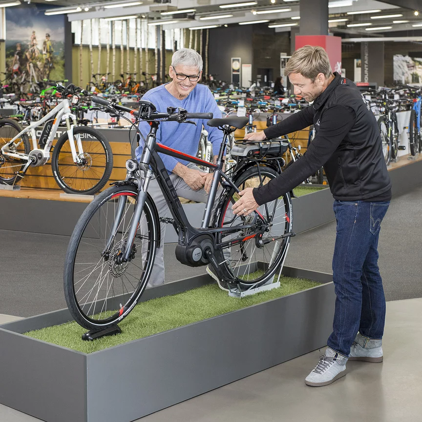 Un consulente Bosch eBike si trova con un uomo in un negozio di biciclette davanti a una bici esposta e gliela spiega.