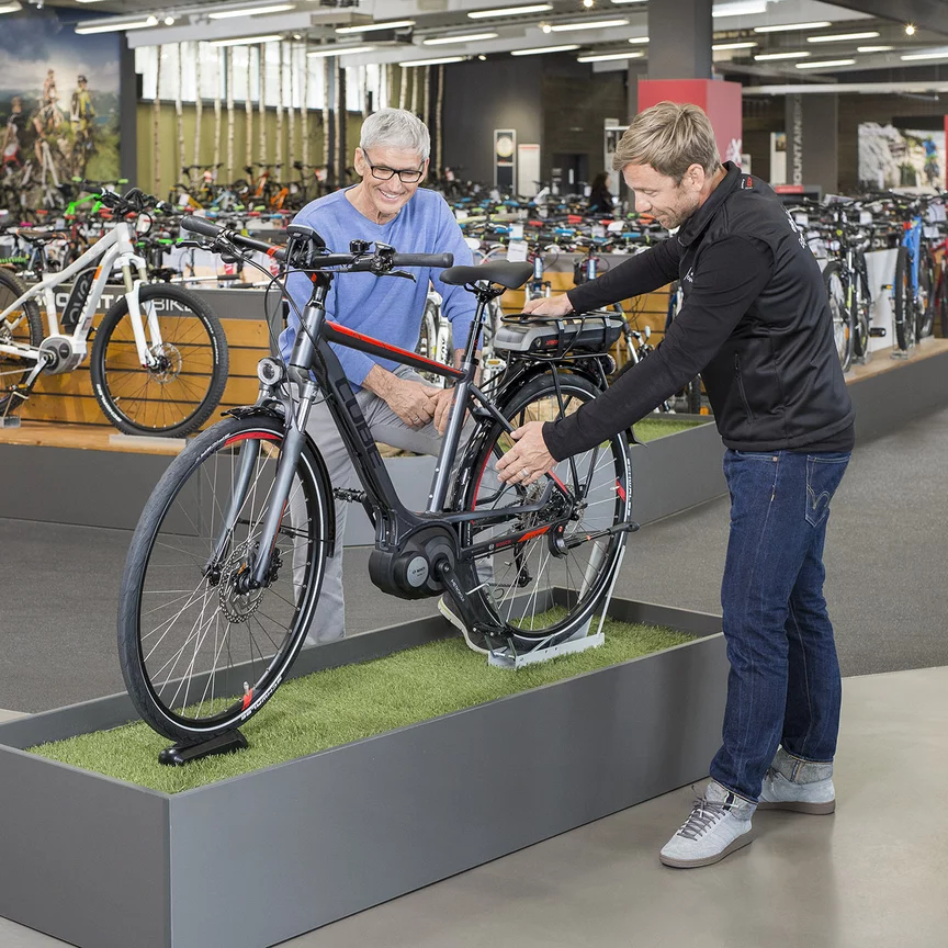 Konsultant Bosch rower ze wspomaganiem elektrycznym / e-rower stoi z mężczyzną przy rowerze wystawowym w sklepie rowerowym i wyjaśnia mu szczegóły.