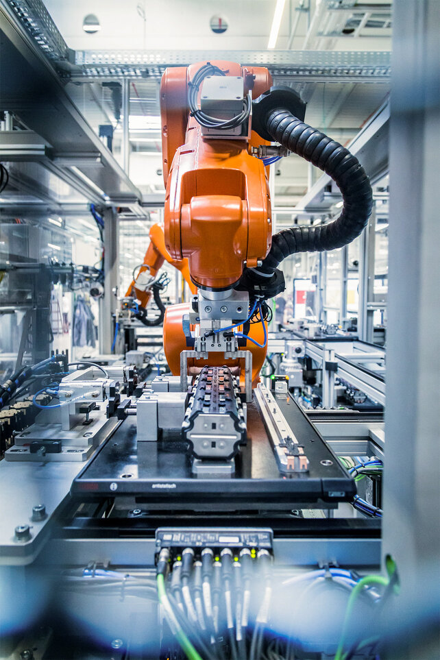 Roboter fügt mehrere Zellblöcke zusammen, im Hintergrund ist ein Fabrik-Innenraum zu sehen.