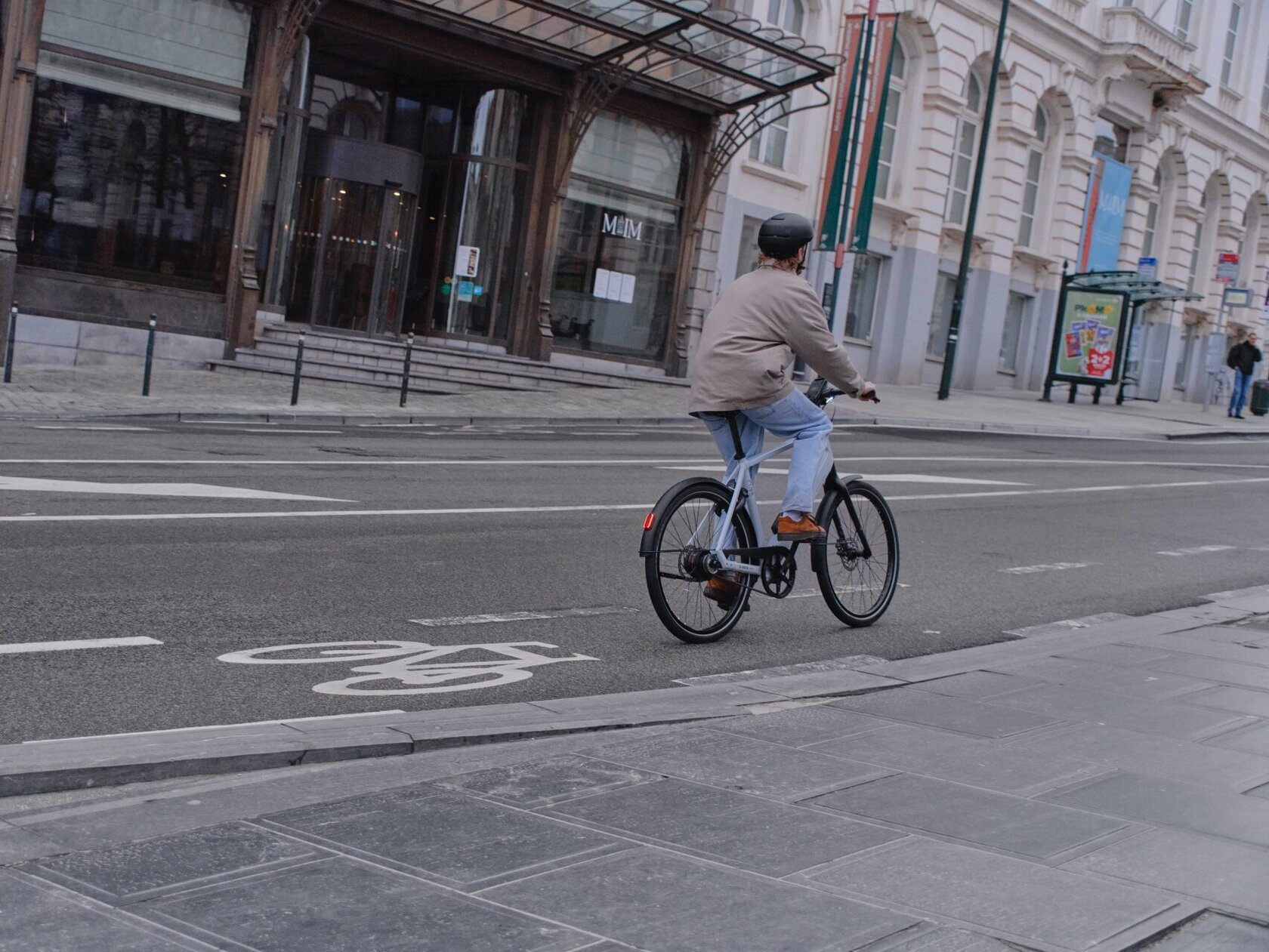 Un ciclista circula por una calle ancha en una ciudad, visto desde atrás, por un carril bici señalizado. El eBike blanco está equipado con un motor de cubo de Bosch.