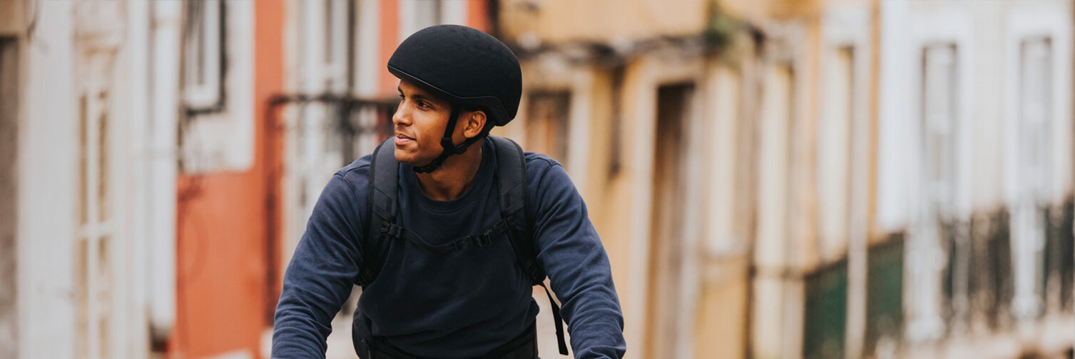 A man is riding his eBike through an alley, glancing to the side. A smartphone is attached to the eBike, with houses visible in the background.