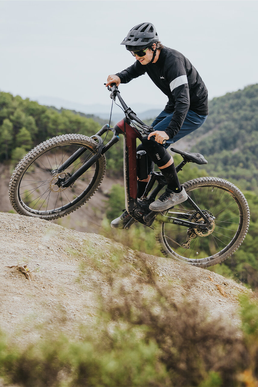 Ein Mann fährt lächelnd auf seinem eMTB durch steiles Gelände in der Natur.