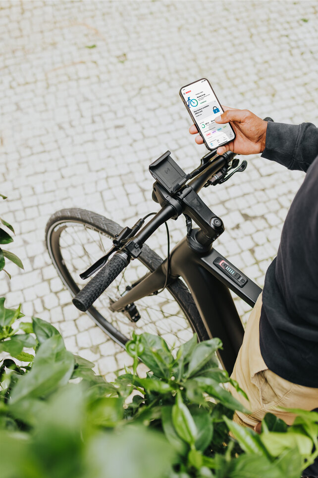 The smartphone is held in one hand, displaying the home page of the eBike Flow app. The other hand is gripping the eBike handlebar.