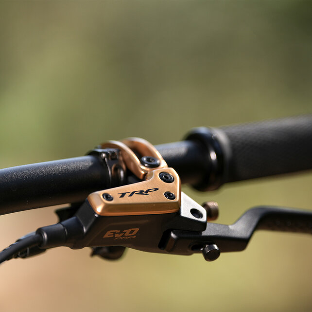 Gros plan sur un guidon de vélo équipé d'un frein TRP EVO Pro en or métallisé avec des accents noirs.