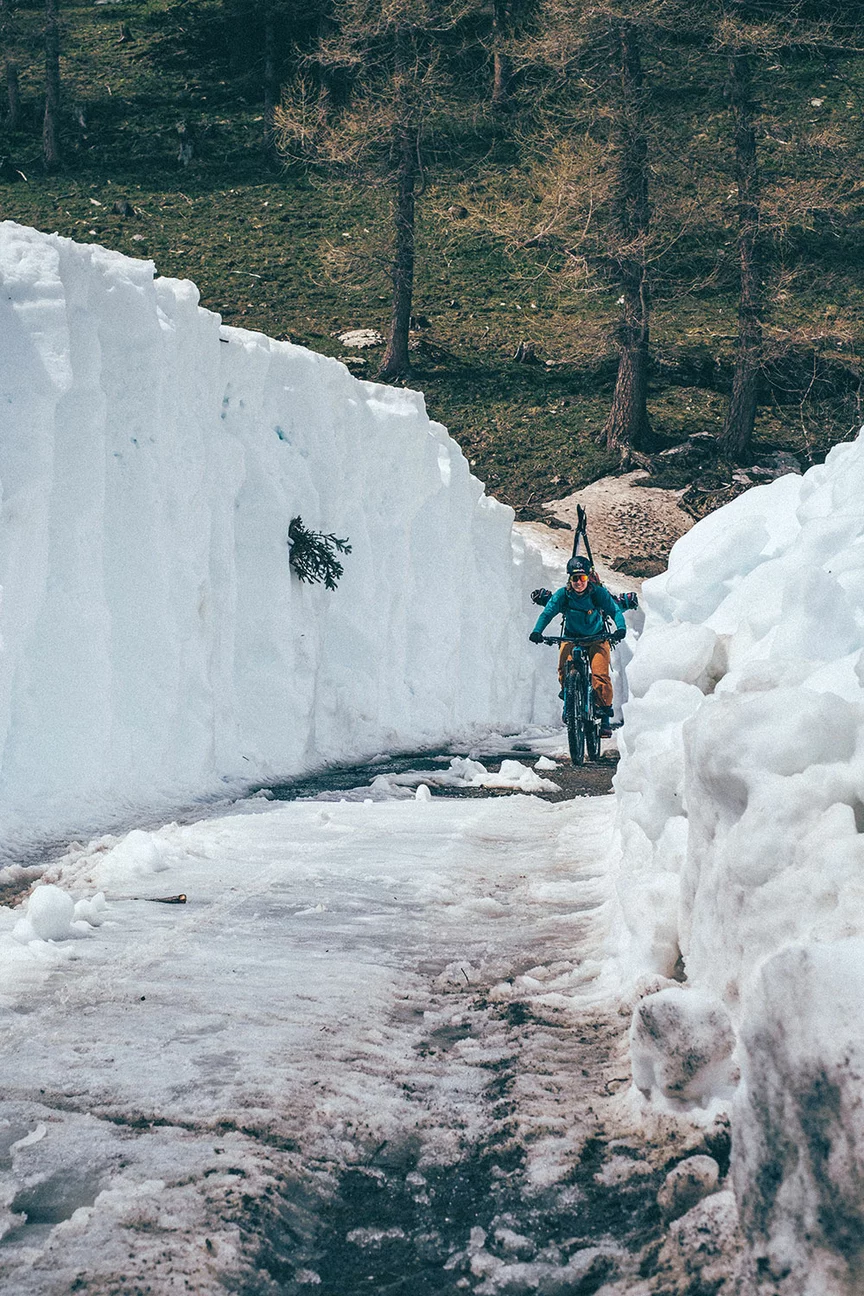 Un utilisateur de VAE / cycliste / sportif à VAE roule sur un chemin enneigé, entouré de hauts murs de glace à gauche et à droite. Des arbres et de l’herbe apparaissent en arrière-plan.