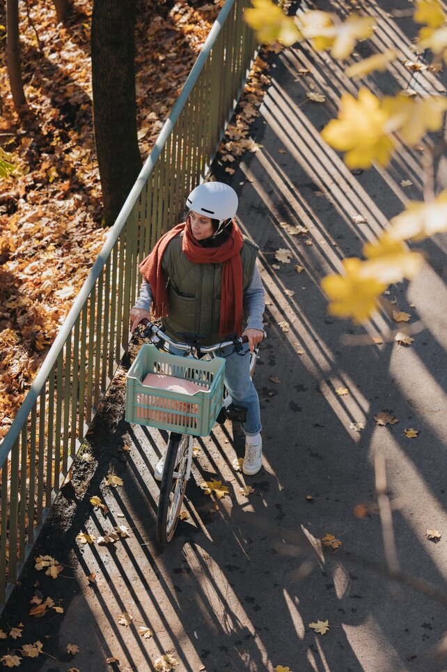 pohled shora na cyklostezku, kde stojí žena s bílým eBike a červeným šátkem. Na cestě a vedle ní jsou listy.