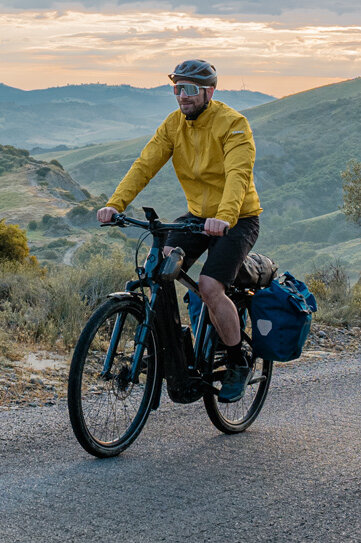 Kobieta i mężczyzna jadą rowerami eTrekking po drodze, w tle rozległy krajobraz.