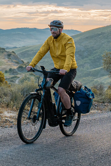 En kvinne og en mann sykler på sine eTrekking-bikes på en vei, med et vidstrakt landskap i bakgrunnen.
