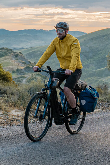 Una mujer y un hombre recorren la carretera en sus eTrekking, con un amplio paisaje de fondo.