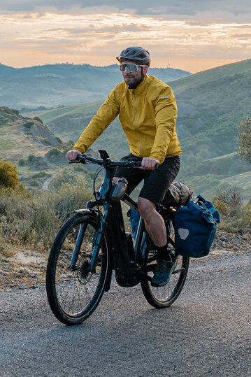 En kvinna och en man cyklar på en väg med sina eTrekking-bikes, med ett vidsträckt landskap i bakgrunden.
