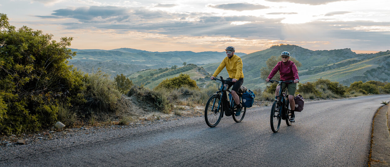 Une femme et un homme roulent sur une route avec leurs eTrekking-Bikes, un vaste paysage en arrière-plan.
