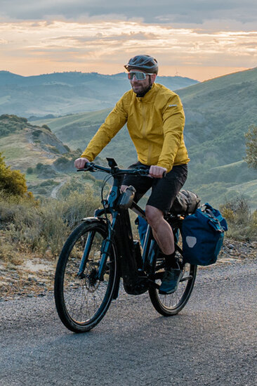 Una donna e un uomo percorrono una strada con le loro bici eTrekking, con un ampio paesaggio sullo sfondo.