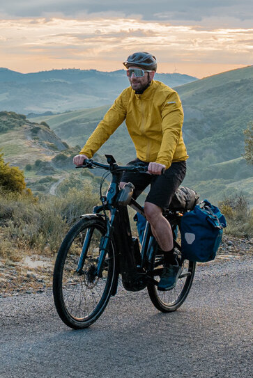 Žena a muž jedou na svých eTrekking bikách po silnici s rozlehlou krajinou v pozadí.