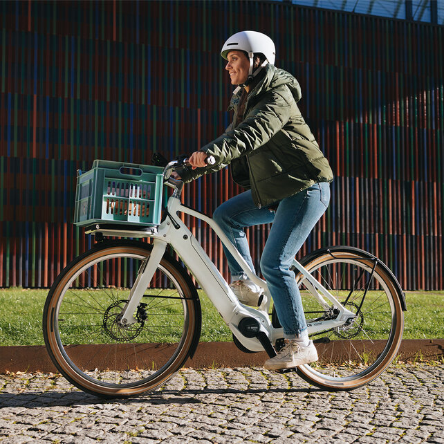 A woman wearing a helmet rides her white eBike along a cobbled street.