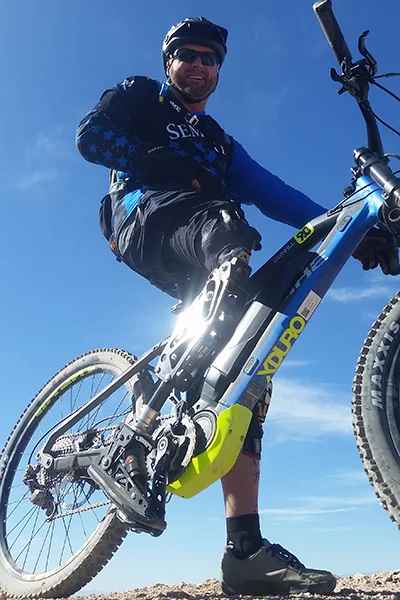 An eMountain bike rider on his eBike, one foot on the ground, is photographed from below and looks into the camera.