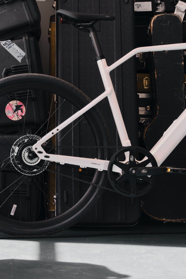Un eBike blanco de Canyon con un motor de cubo de Bosch está aparcado en una zona entre bastidores. Al fondo, se apilan cajas de transporte negras y cajas de instrumentos.