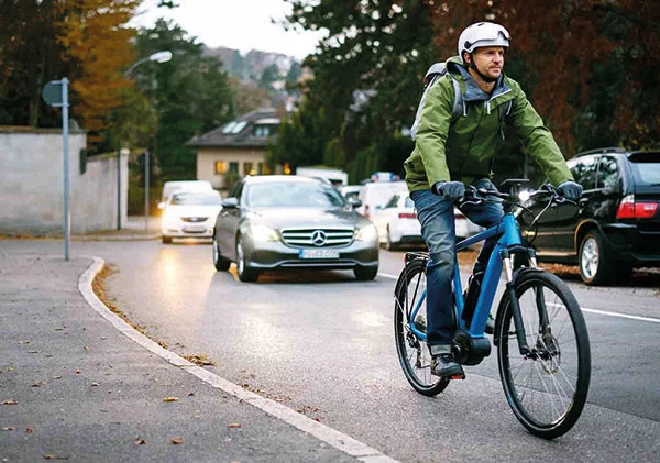A man in a green jacket is riding an eBike on a bustling city street.