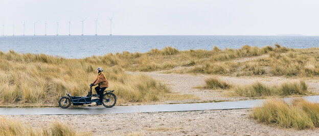 Vrouw rijdt met een eCargo fiets langs de kust in Kopenhagen.