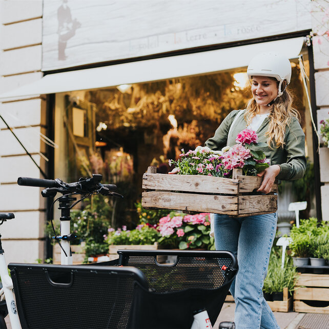 Une femme porte une caisse en bois remplie de fleurs roses jusqu’à son VAE Cargo.