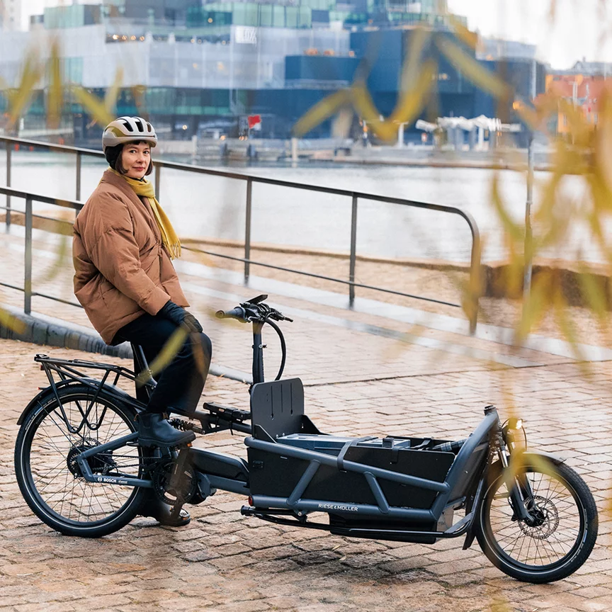 Sofie Birc steht auf ihrem Lastenrad und schaut in die Kamera, im Hintergrund sind der Hafen und Gebäude zu erkennen.