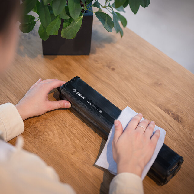 A Bosch CompactTube 400 lies on a wooden table and is gently wiped with a cloth.