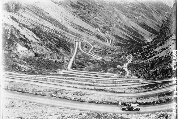 Scatto in bianco e nero di un paesaggio montano con una strada su cui viaggia un veicolo elettrico.