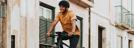 A man wearing a helmet rides an eBike through an alley, smiling as he goes.