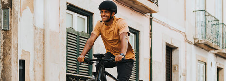 A man wearing a helmet rides an eBike through an alley, smiling as he goes.