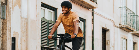 A man wearing a helmet rides an eBike through an alley, smiling as he goes.